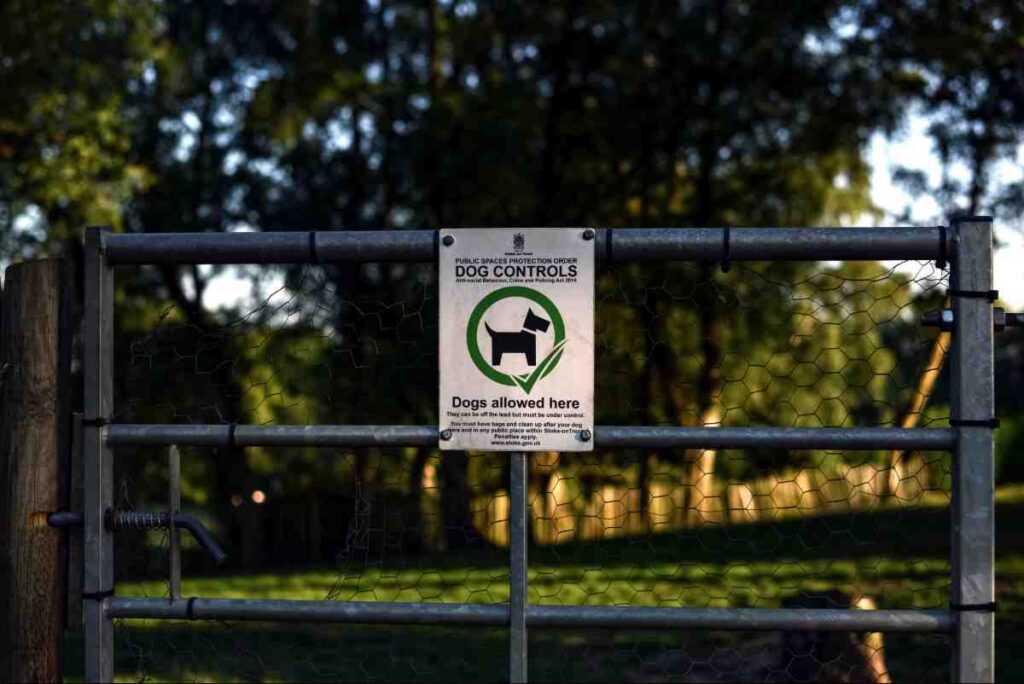 Invisible Fence HOA Rules — Dog Controls sign posted on a metal gate near a park