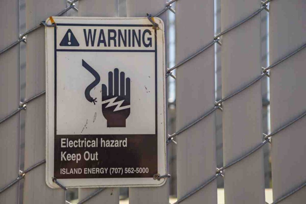 Electrical hazard warning sign on a metal fence highlighting invisible fence risks